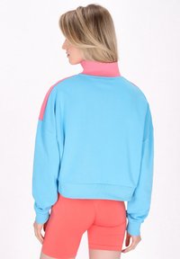 Sudadera de corte relajado con un cuerpo azul y cuello rosa, con puños acanalados. Combinada con pantalones cortos coral, que muestran un diseño deportivo.