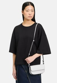 Czarna, oversize t-shirt z okrągłym dekoltem, w połączeniu z białą, skórzaną torbą na ramię z klapą i regulowanym paskiem.