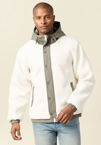 Biała polarowa kurtka z khaki kapturem, rombowym pikowaniem z przodu, z zatrzaskami i elastycznymi mankietami. Nosi się ją na dżinsy.