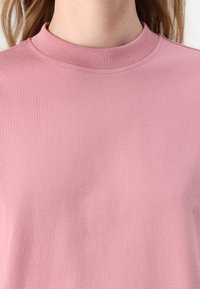 Rosa bomull t-skjorte med ribbet crew-hals. Glatt tekstur, korte ermer og minimal detaljering på stoffet. Standard passform.