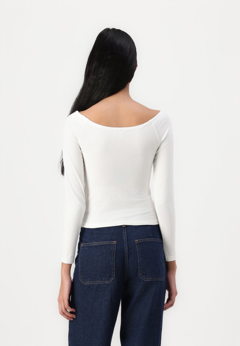 Maglietta bianca a maniche lunghe con scollatura ampia, abbinata a jeans blu in denim a vita alta con tasche posteriori e vestibilità dritta.