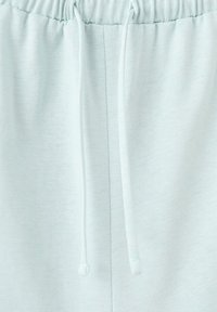 Ceinture élastique bleu clair avec deux cordons suspendus en tissu doux, probablement partie d'un vêtement décontracté comme un pantalon de survêtement ou un short.