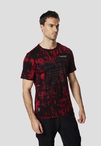Červené a černé grafické tričko s abstraktními texturami, krátkými rukávy, kulatým výstřihem a potiskem značky na přední straně.