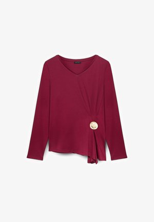 Bordeaux langærmet top med V-hals, med en sidesløjfe og en dekorativ cremefarvet knap. Stoffet ser blødt og strækbart ud.