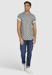 Kurzes Hemd mit einem bunten Blumenmuster, weißen Manschetten, kombiniert mit dunkelblauen Jeans und weißen Sneakers. Lässig, entspannte Passform.