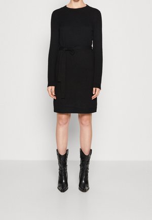 Abito in maglia nera con scollatura rotonda, maniche lunghe e cintura in tessuto. Indossato con stivali cowboy neri a punta, con una finitura testurizzata.