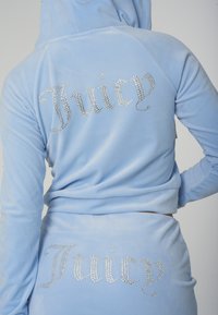 Fato de treino em veludo azul claro com "Juicy" escrito em brilhantes pedras de strass nas costas do casaco com capuz e calças combinando.