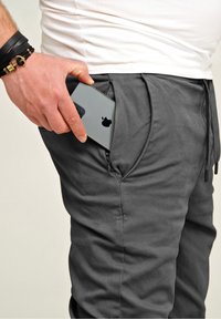 Gray jogger pants with a smooth texture, featuring a zippered pocket. A hand is placing a smartphone into the pocket.
