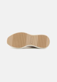 Såle av en DKNY sneakers, med en teksturert beige gummibase med horisontale spor og en hvit kant. Klar merkevare på hælen.