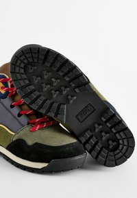 Wielokolorowe buty trekkingowe z zamszowymi i materiałowymi elementami, okrągłe czerwone sznurówki, teksturowana czarna gumowa podeszwa oraz warstwowy design z akcentami.