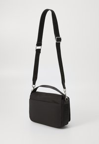 Sort nylon skuldertaske med justerbar rem, rektangulær form, glat tekstur, med en sølvfarvet hardware-lukning og brandede detaljer.