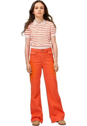 Pantalones de mezclilla acampanados de color naranja con bolsillos delanteros, combinados con una camiseta tipo polo a rayas blancas y rojas, de manga corta y cuello.