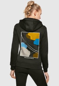 Black hoodie featuring a colorful abstract design on the back with yellow, blue, and gray shapes, and "UNLIMITED SKILLS" text.