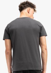Mørkegrå kortærmet t-shirt lavet af bomuld. Har en rund halsudskæring og et lille mærke på venstre side nær sømmen.