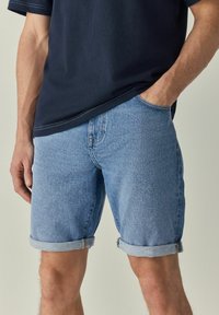 Denim šorts u svijetloplavoj boji, s preklopom na rubu i prednjim džepovima. Tkanina ima blago teksturiranu površinu i ležeran kroj.