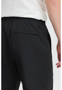 Pantalones de chándal negros con cintura elástica, que cuentan con un bolsillo trasero y una tela suave y texturizada. El ajuste es holgado y casual.