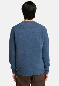 Blå ribbad tröja med en texturerad yta, rund halsringning och långa ärmar. Har raglanärmar och en rak fåll.