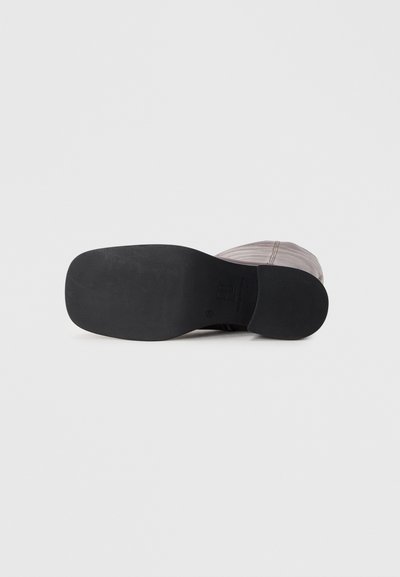Black flat shoe sole with a smooth texture and rounded shape. Features a subtle patterned base and minimal branding. Light-colored upper.