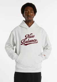 Felpa grigia con un grande logo bordeaux "New Balance". Presenta una tasca frontale, un cappuccio spazioso e polsini a coste per una vestibilità comoda.