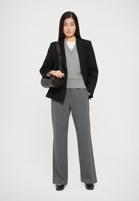 Schwarzer taillierter Blazer, grauer V-Ausschnitt-Pullover, graue weit geschnittene Hose und eine runde dunkle Handtasche. Glatter Stoff mit einer strukturierten Silhouette.