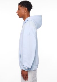 Helleblaue Pullover-Hoodie aus weichem Material, mit einer Kängurutasche, gerippten Bündchen und einer verstellbaren Kapuze. Schlichtes, minimalistisches Design.