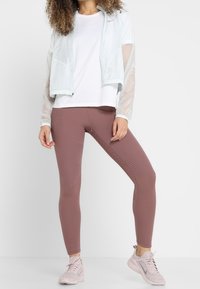 Lichtblauwe ritsjack met transparante mouwen, witte t-shirt, geribde bruine leggings en lichtroze sneakers. Gladde materialen, sportief ontwerp.