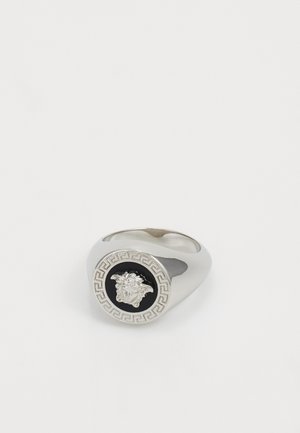 Zilveren ring met een zwart, cirkelvormig middenstuk met een gedetailleerd ontwerp van een Medusa-hoofd, omringd door een Grieks sleutelpatroon. Soepele, gepolijste afwerking.