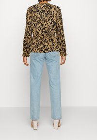 Blusa marrone con stampa leopardata, maniche a sbuffo, vita cinte, abbinata a jeans dritti azzurri e tacchi chiari.