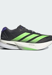 Baskets de course noires avec un design rayé vert et noir, tige en mesh léger, accents violets, semelle intermédiaire blanche et semelle extérieure texturée.