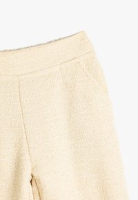 Texturierte cremefarbene Hose aus einem weichen, gewebten Stoff; verfügt über einen elastischen Bund und seitliche Taschen.