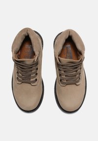 Botines de ante beige con puntera redonda. Las características incluyen cordones marrón oscuro, suelas de goma texturizadas y un cuello acolchado para mayor comodidad.