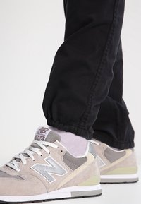 New Balance 996 sneakers, met bovenwerk van grijs suède en mesh, witte veters en een gevoerde zool met een lichtgroene accent. Zwarte broek zichtbaar.