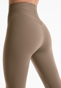 Bruine high-waisted leggings van rekbaar materiaal, met een gestructureerde tailleband met diagonale lijnen en een gladde afwerking.