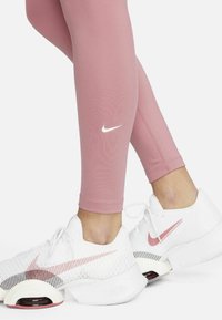 Rosa åtsittande leggings med en vit Nike-logga, i kombination med vita sneakers som har en texturerad ovandel och rosa accentdetaljer.