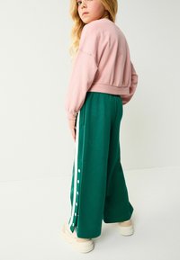 Sweatshirts courts roses et pantalons larges verts avec des boutons latéraux blancs. Textures douces, coupe décontractée et chaussures légères.