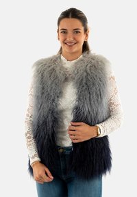 Gilet in pelliccia sintetica con sfumatura dal grigio al blu navy, caratterizzato da una texture morbida. Indossato sopra un top in pizzo bianco, abbinato a jeans blu.