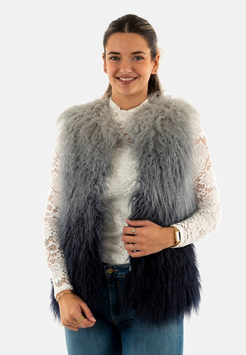 Gilet in pelliccia sintetica con sfumatura dal grigio al blu navy, caratterizzato da una texture morbida. Indossato sopra un top in pizzo bianco, abbinato a jeans blu.