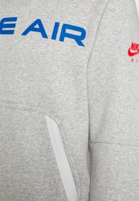 Gray sweatshirt featuring bold blue "AIR" lettering and a red Nike logo. Smooth texture with a white zippered pocket detail.