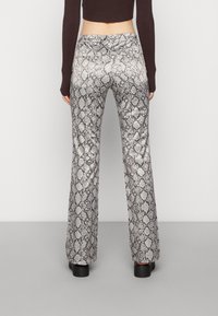 Spodnie z wysokim stanem, rozszerzane na dole, w wzór węża. Teksturowany srebrno-czarny wzór z błyszczącym wykończeniem. Widoczne solidne czarne platformy.