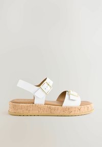 Sandales à plateforme blanches avec semelle en liège, bride ajustable avec accents de boucle en or, design ouvert à l'avant et upper lisse en simili cuir.