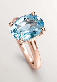 Anillo de oro rosa con una piedra preciosa ovalada de color azul claro sujeta por cuatro garras. Banda suave y pulida con un acabado brillante.