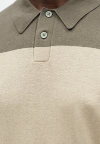 Πολυτονική πλεκτή πόλο μπλούζα με μπλοκ χρωμάτων σε μπεζ και ελιά, διαθέτοντας γιακά και δύο κουμπιά στο κλείσιμο.