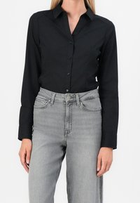 Camicia nera a maniche lunghe con colletto, abbinata a jeans a vita alta grigi chiari con tasche e un bottone a contrasto.