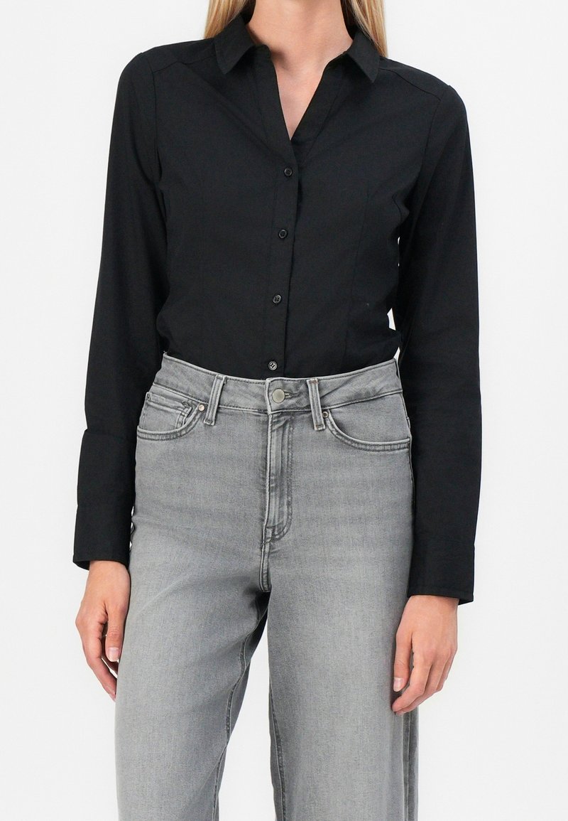 Camicia nera a maniche lunghe con colletto, abbinata a jeans a vita alta grigi chiari con tasche e un bottone a contrasto.