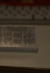 Etichetă de îngrijire a textilelor care include diverse limbi, afișate cu negru pe un fundal de țesătură albă, având o textură mată și o ușoară strălucire.