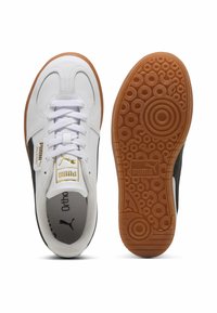 Baskets de sport blanches et noires avec une semelle en caoutchouc marron, une tige texturée, un système de laçage, et des accents dorés affichant le logo Puma.