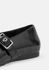Shoe plano de verniz preto com bico redondo, uma tira lateral com fivela e um acabamento liso e brilhante. Sola plana para conforto.
