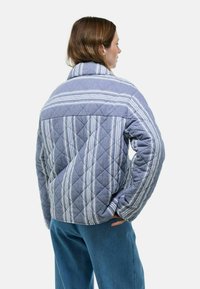 Veste matelassée en tissu bleu avec des rayures diagonales et horizontales. Présente un col montant et une coupe décontractée. Surface texturée et manches longues.