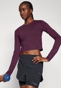 Long-sleeve, cropped, maroon top paired with black shorts. The top features a round neckline; shorts have an elastic waistband and logo detail.
