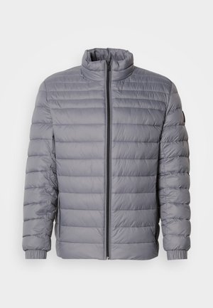 Siva podložena jakna z visokim ovratnikom, zadrgo, horizontalnim prešitjem in elastičnimi manšetami. Lahkotna material poudarja toplino.